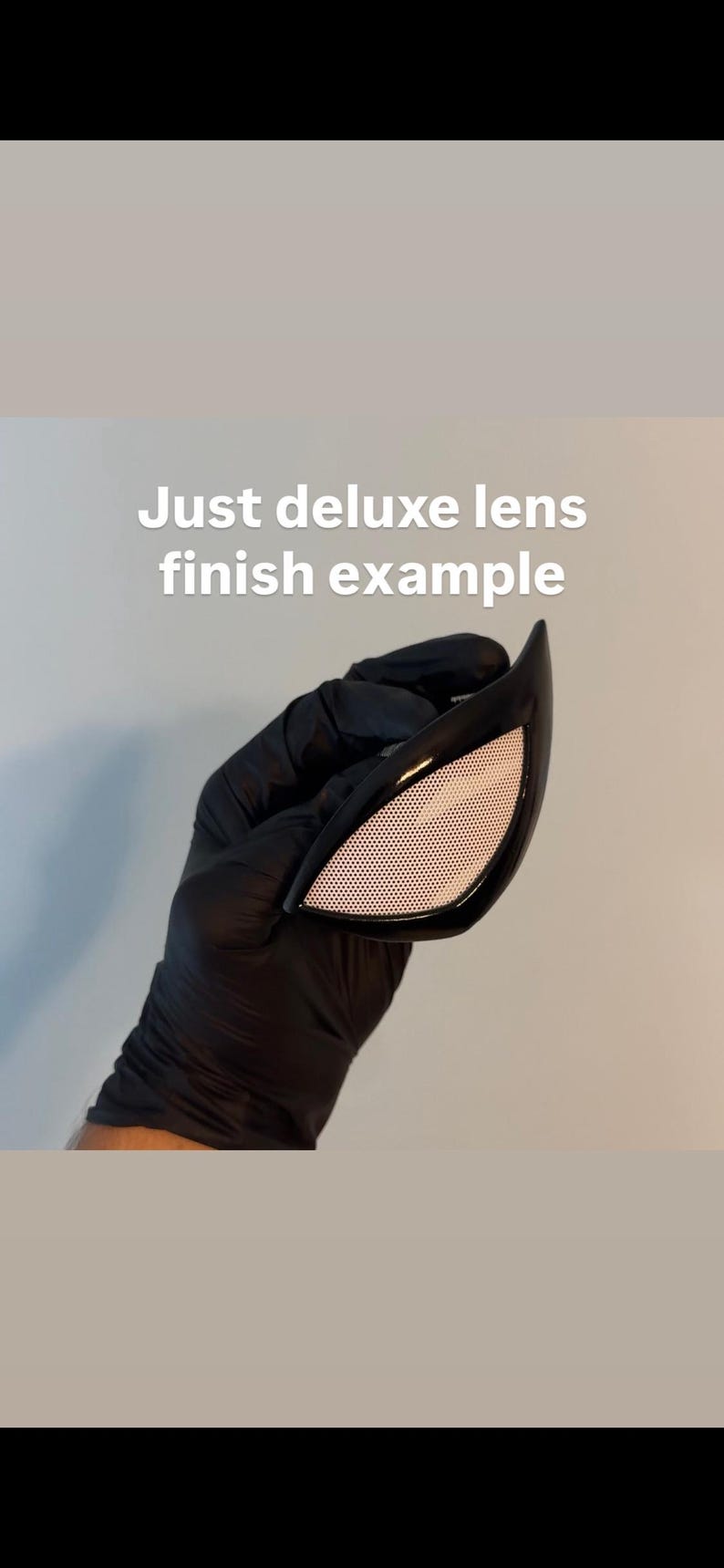 Op de afbeelding: Zwarte Spiderman-stijl ooglens met een wit mesh-patroon. De tekst "Just deluxe lens finish example" wordt in het wit weergegeven. De lens wordt vastgehouden door een gehandschoende hand.