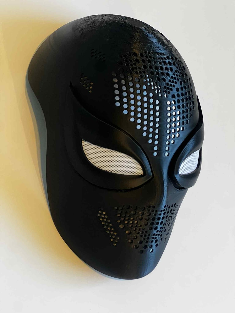 Puede incluir: Una m&aacute;scara negra con una superficie texturizada y aberturas para los ojos cubiertas con malla blanca. La m&aacute;scara tiene una serie de peque&ntilde;os agujeros en la parte superior y los lados. La m&aacute;scara es probablemente para cosplay o disfraces.