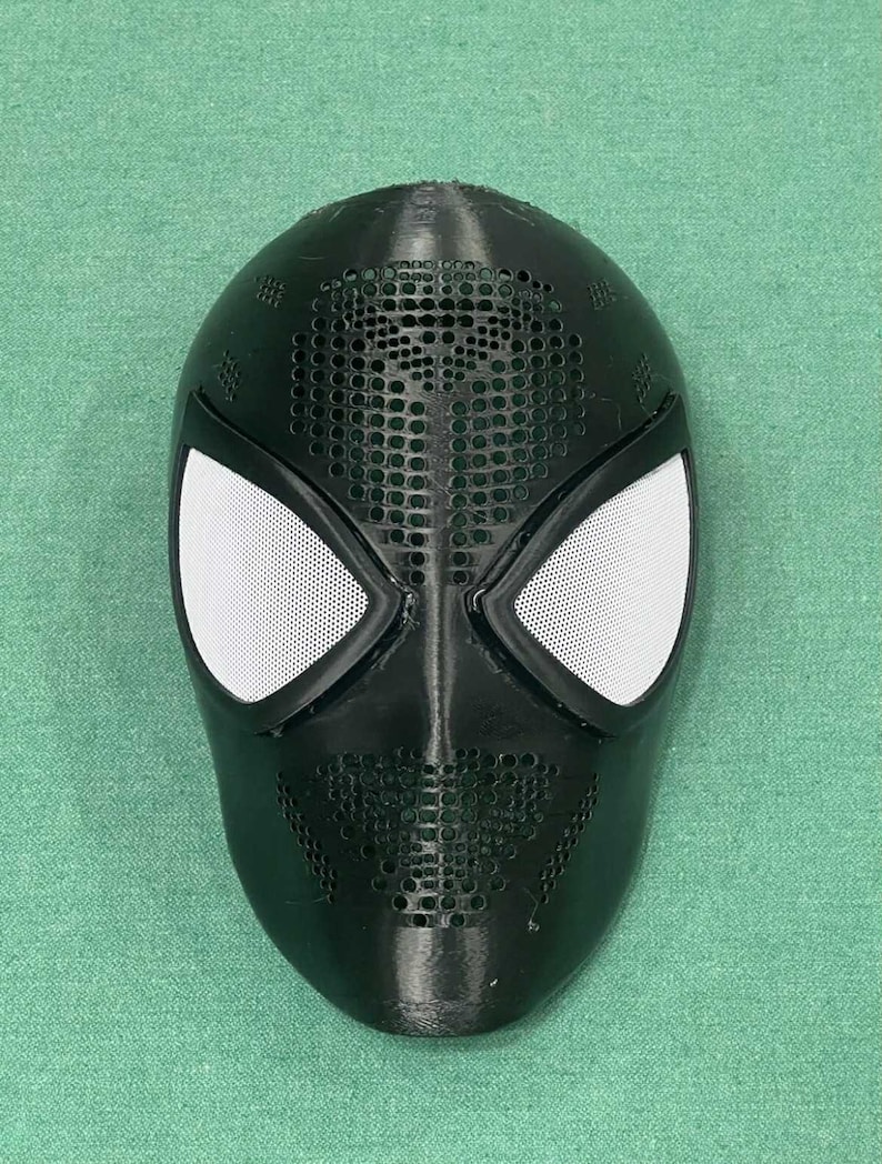 May include: Black Spider-Man mask with white mesh eye coverings and a perforated design on the forehead and mouth area. The mask is made of a matte black material and is likely a costume accessory.