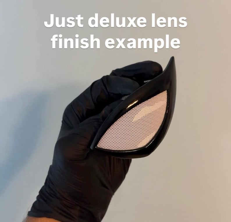Puede incluir: Una lente negra con acabado de lujo y malla blanca punteada. El texto "Just deluxe lens finish example" se muestra en blanco. La lente est&aacute; sujeta por una mano enguantada.