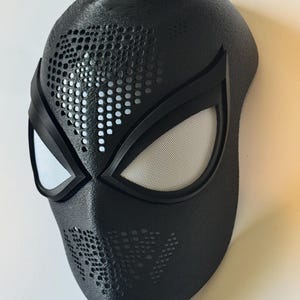 Puede incluir: Una m&aacute;scara negra con una superficie texturizada, con grandes aberturas para los ojos con malla blanca y ribete negro. La m&aacute;scara tiene una serie de peque&ntilde;as perforaciones circulares y est&aacute; dise&ntilde;ada para parecerse a una m&aacute;scara de superh&eacute;roe.