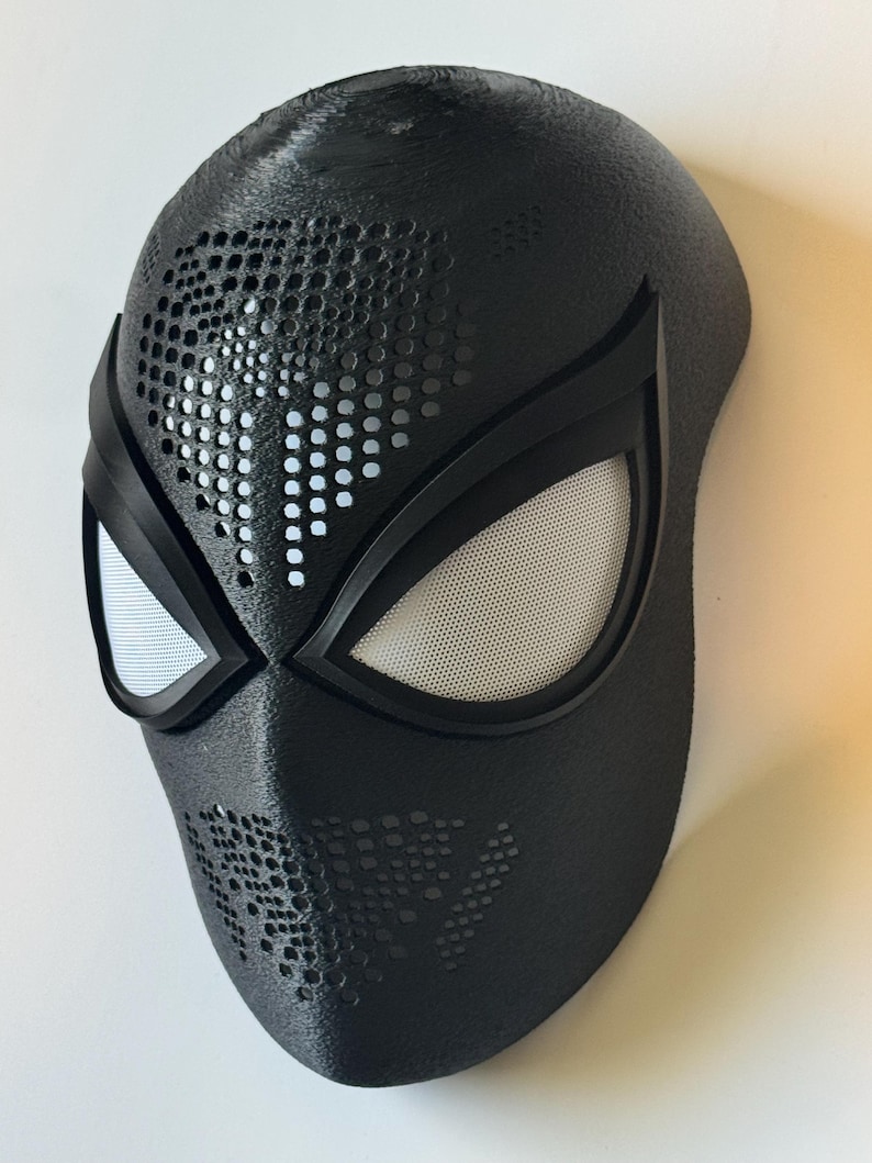 Puede incluir: Una m&aacute;scara negra con una superficie texturizada, con grandes aberturas para los ojos con malla blanca y ribete negro. La m&aacute;scara tiene una serie de peque&ntilde;as perforaciones circulares y est&aacute; dise&ntilde;ada para parecerse a una m&aacute;scara de superh&eacute;roe.