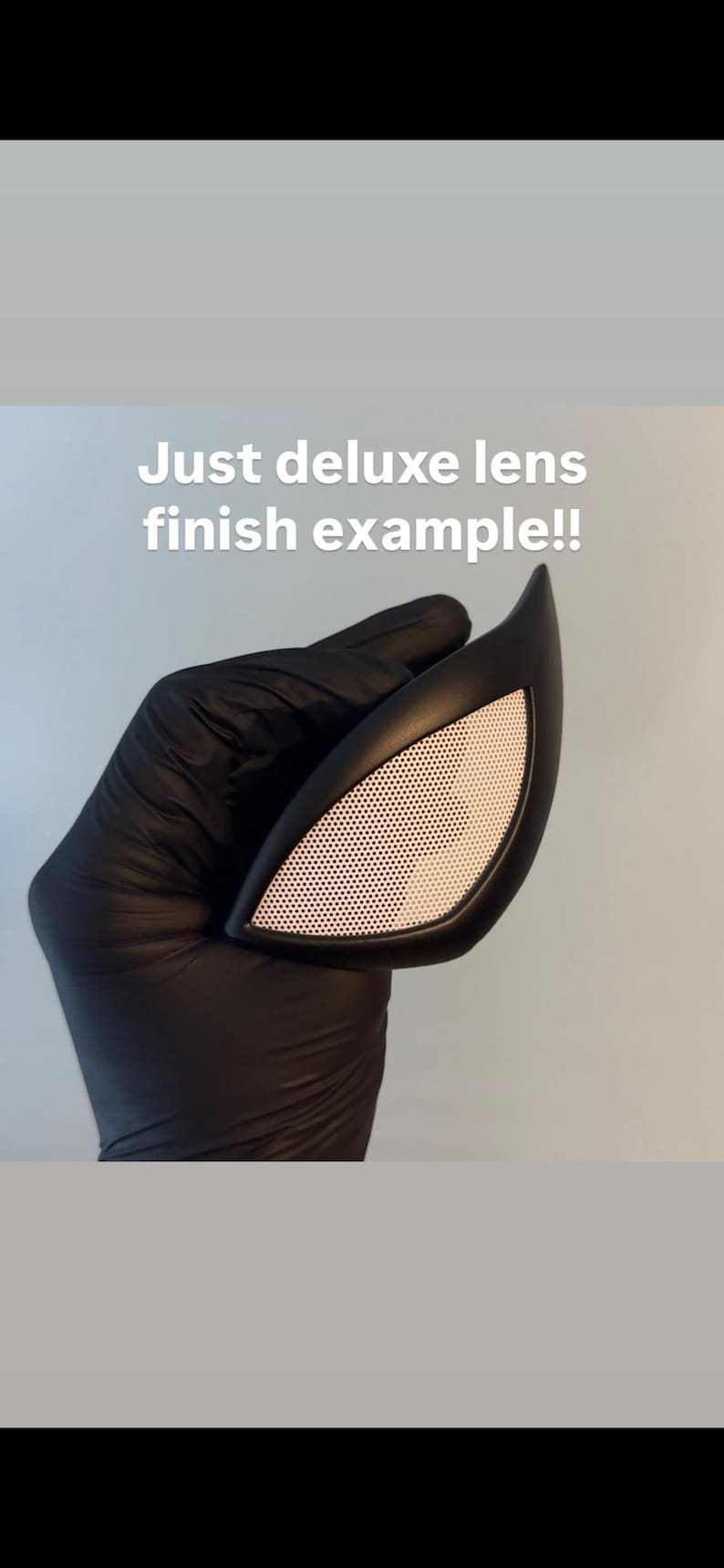 Op de afbeelding: Een zwarte, hoekige maskerlens met een wit, geperforeerd lensgedeelte. De tekst "Just deluxe lens finish example!!" wordt in het wit weergegeven. De lens wordt vastgehouden door een gehandschoende hand.