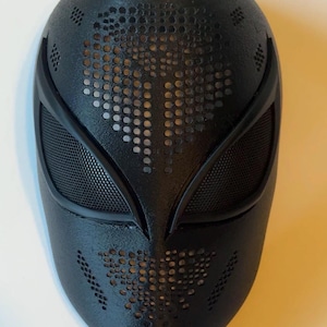 May include: A black mask with a textured surface and a design of small holes. The mask has eye openings with mesh and a pattern of holes across the forehead and chin. The mask is likely for cosplay or costume use.