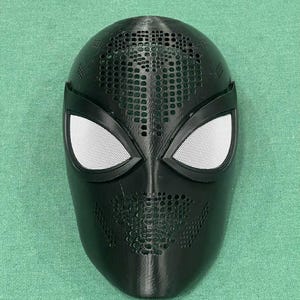 May include: A black mask with white mesh eye coverings. The mask has a textured surface with small circular perforations across the top and lower face. The mask is likely for cosplay or costume use.