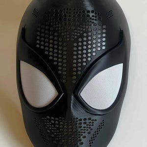May include: A black Spider-Man mask with white mesh eye coverings. The mask has a textured surface and a pattern of small holes across the face. A superhero costume accessory.