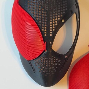 Pu&ograve; includere: Maschera nera e rossa dal design distintivo. La maschera presenta una base nera con un motivo perforato e una copertura per gli occhi rossa a forma di rete. Probabilmente per cosplay o costumi.