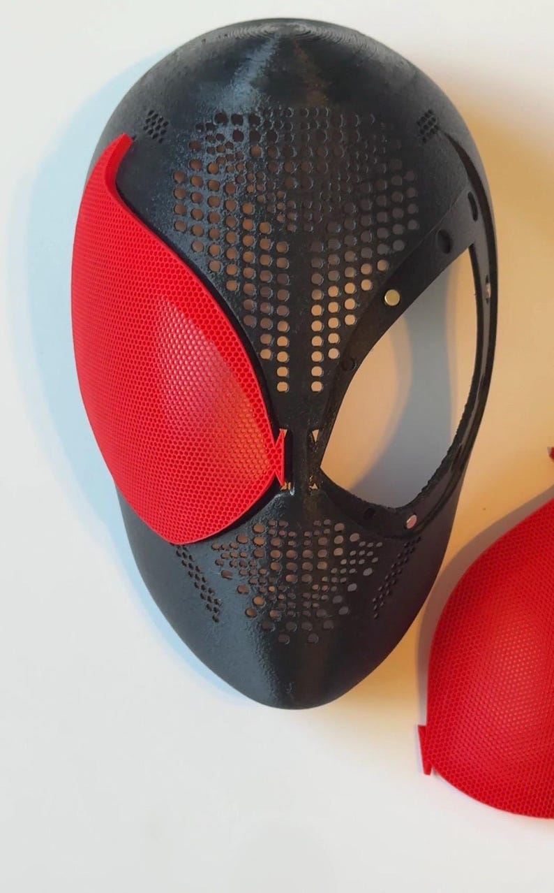 Pu&ograve; includere: Maschera nera e rossa dal design distintivo. La maschera presenta una base nera con un motivo perforato e una copertura per gli occhi rossa a forma di rete. Probabilmente per cosplay o costumi.
