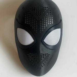 Op de afbeelding: Een zwart masker met witte mesh oogbedekkingen. Het masker heeft een textuur met een patroon van kleine gaatjes over het voorhoofd en de mond. Het masker is ontworpen om het hele gezicht te bedekken.