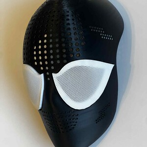 Puede incluir: Una m&aacute;scara de Spider-Man en blanco y negro con una superficie texturizada. La m&aacute;scara presenta cubiertas oculares de malla blanca y un dise&ntilde;o perforado en las secciones superior e inferior. La m&aacute;scara est&aacute; dise&ntilde;ada para cubrir la cara.