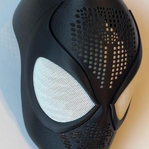 Op de afbeelding: Een zwart superheldenmasker met witte mesh oogbedekkingen. Het masker heeft een getextureerd oppervlak en is geperforeerd met kleine gaatjes rond de mond en het voorhoofd. Het is een cosplay-item.