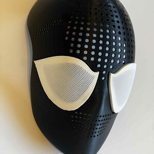 Puede incluir: Una m&aacute;scara negra con cubiertas oculares de malla blanca. La m&aacute;scara tiene una serie de peque&ntilde;os agujeros espaciados uniformemente en la parte superior y los lados. Las cubiertas oculares son de un blanco brillante, contrastando con el negro.
