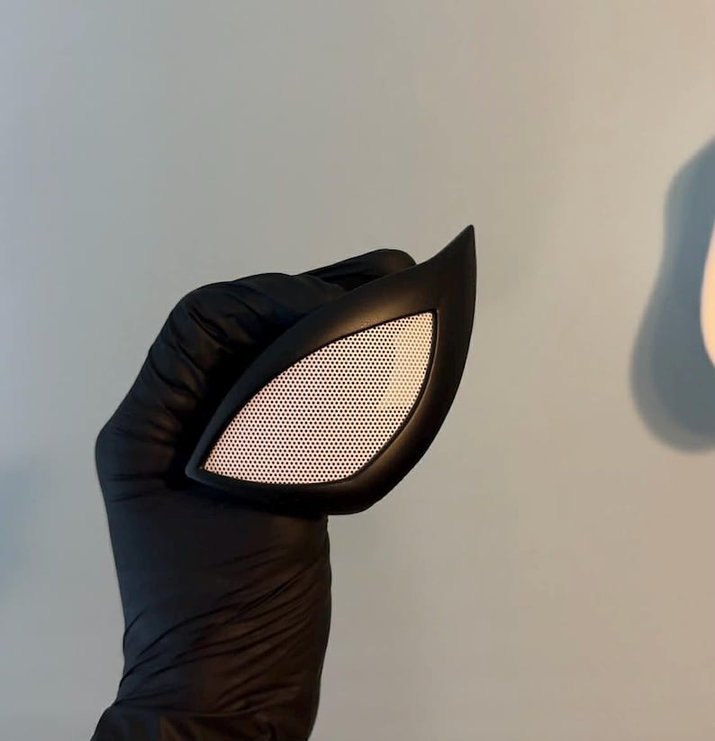 May include: A single eye lens piece for a mask, featuring a sharp, angular black frame surrounding a white mesh screen. The lens has a distinct almond shape with a pointed outer corner, designed with a smooth matte finish on the frame.