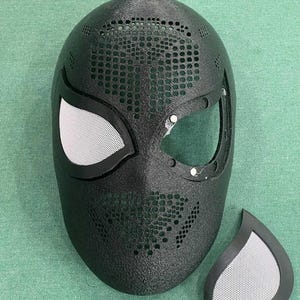 May include: A black, textured mask with white mesh eye coverings and a separate matching eye piece. The mask has a perforated design and is likely for cosplay or costume use.