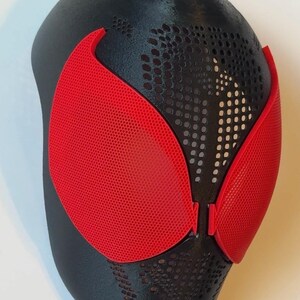 Pu&ograve; includere: Una maschera nera e rossa con una superficie strutturata. La maschera presenta copriocchi rossi e un design perforato nella parte superiore. Probabilmente &egrave; un accessorio per costumi o cosplay.