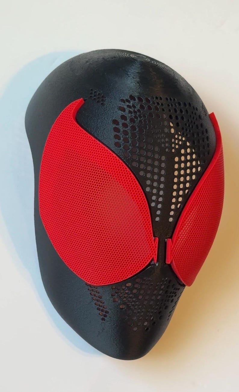 Pu&ograve; includere: Una maschera nera e rossa con una superficie strutturata. La maschera presenta copriocchi rossi e un design perforato nella parte superiore. Probabilmente &egrave; un accessorio per costumi o cosplay.