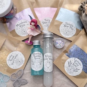 May include: A collection of fantasy-themed bath products, including bath salts, fizz, and bubble brew, in various colours and packaging. A small fairy figurine and decorative butterflies are also present. The products are labelled with fantasy-themed names.