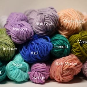May include: A collection of yarn skeins in various colors, including teal, aqua, silver, lilac, blush, emerald, moss, and warm peach. Each skein is labeled with a color name.