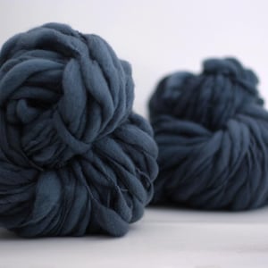 May include: Two large, navy blue arm knitting yarn balls are displayed against a white background. The yarn is thick and chunky, perfect for creating cozy blankets or scarves. The texture of the yarn is clearly visible.