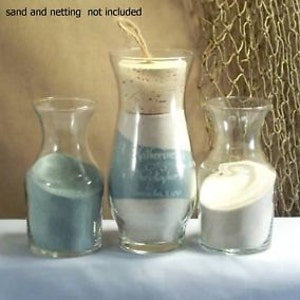 May include: Three glass vases with different colored sand inside. The vases are clear glass and have a rounded shape. The sand is blue, white, and beige.