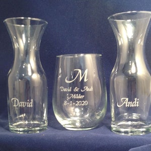 May include: Two clear glass decanters with the names "David" and "Andi" etched on them, and a clear glass wine glass with the names "David & Andi" and the date "8-1-2020" etched on it.