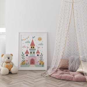 K&ouml;nnte beinhalten: Gerahmte Illustration eines skurrilen Schlosses mit rosa, blauen und gelben Akzenten, Flaggen und einer l&auml;chelnden Sonne. Ein gro&szlig;er Teddyb&auml;r mit gelbem Herz sitzt in der N&auml;he. Ein Baldachin mit goldenen Sternen h&auml;ngt &uuml;ber einem rosa Bodenkissen.