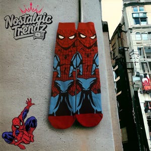May include: Pair of red, blue, and black Spider-Man socks. The socks feature a detailed graphic of Spider-Man's costume. The socks are displayed against a gray wall with the text "Nostalgic Trendz" and a Spider-Man sticker.