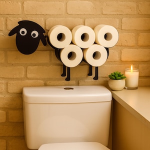 May include: A novelty black metal toilet roll holder in the shape of a sheep, mounted on a brick wall. The holder is designed to hold six toilet rolls, arranged to form the sheep's body. The sheep has a head with white eyes and black legs.