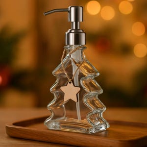 May include: Clear glass soap dispenser in the shape of a Christmas tree with a silver pump and a wooden star-shaped tag. The dispenser is on a wooden tray, with a blurred background of warm, out-of-focus lights.
