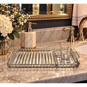 May include: A rectangular clear glass tray with a ribbed surface and a beaded edge, featuring integrated handles on the sides. A small, clear glass tumbler sits on the right side of the tray, which is positioned on a white marble countertop.