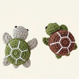 May include: Two handmade crochet turtle toys. One turtle has a green shell with white accents and grey limbs and head. The other turtle has a brown shell with white accents and green limbs and head. Both turtles have black eyes.
