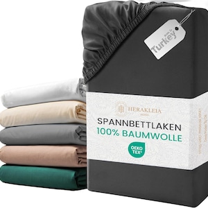 Könnte beinhalten: Ein Stapel gefalteter Spannbettlaken in verschiedenen Farben, darunter Weiß, Beige, Grau und Grün, neben einem dunkelgrauen Spannbettlaken-Set. Das dunkelgraue Set ist mit einem Etikett versehen, auf dem "Made in Turkey" steht. Der Text "SPANNBETTLAKEN 100% BAUMWOLLE" ist ebenfalls zu sehen.