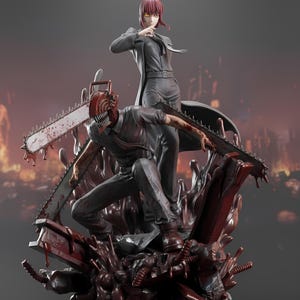 May include: A detailed figurine featuring two characters from the anime series Chainsaw Man. One character is posed with a chainsaw head, the other is standing above. The base is a dark red, textured design with a blurred background.