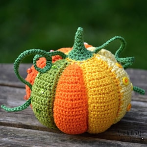 May include: A crocheted pumpkin with green vines and orange, yellow, and green stripes. The pumpkin has small, colorful beads sewn onto it.