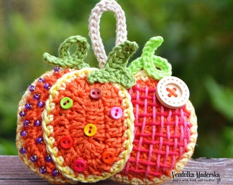 Puede incluir: Un adorno de calabaza de ganchillo con un lazo para colgar. La calabaza es naranja con detalles amarillos y verdes. Tiene una variedad de botones y cuentas de colores.