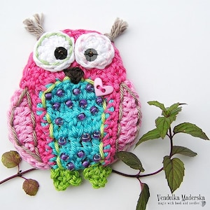 Peut inclure: Un hibou crochet&eacute; &agrave; la main, aux couleurs rose, turquoise et vert. Le hibou a de grands yeux blancs avec des centres noirs, un petit bouton en forme de c&oelig;ur rose et des perles violettes. Le hibou est pos&eacute; sur une branche avec des feuilles vertes.