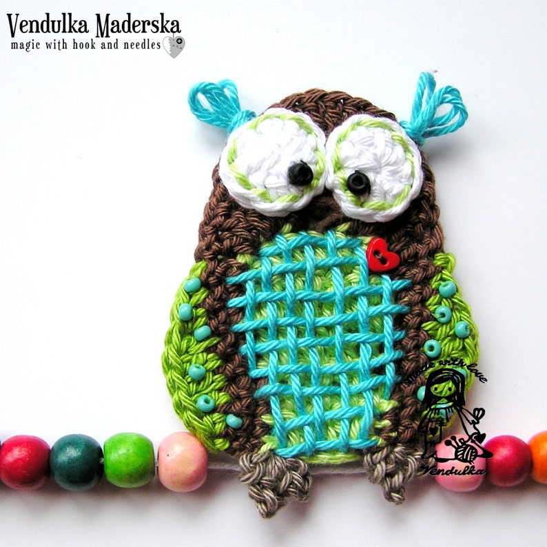 Peut inclure: Applique de hibou crochet&eacute; &agrave; la main, marron, vert et turquoise. Le hibou a de grands yeux blancs avec des pupilles noires, un bouton c&oelig;ur rouge et des perles turquoise. Le texte "Vendulka Maderska" est visible.