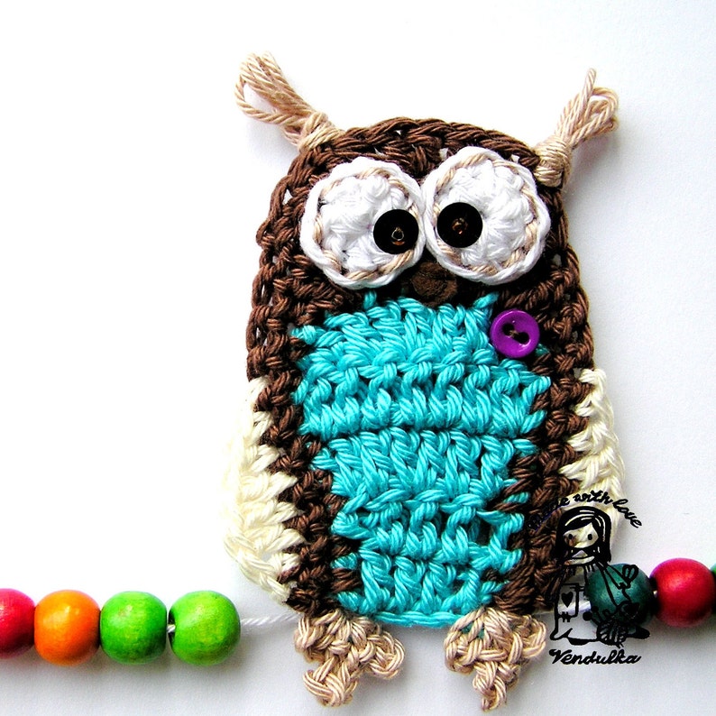 Peut inclure: Un hibou crochet&eacute; &agrave; la main avec du fil marron, blanc et turquoise. Le hibou a de grands yeux en boutons et un bouton violet. Il est attach&eacute; &agrave; une guirlande de perles en bois color&eacute;es. Le design du hibou comprend de petites extensions de fil en forme d'oreilles.