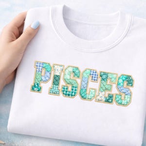 May include: White sweatshirt with the word "PISCES" in a patchwork design. The letters are in shades of blue and green with a gold outline. The sweatshirt is held by a person with light blue nail polish.