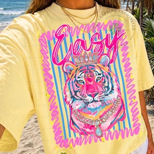 May include: Yellow t-shirt with a colorful tiger graphic wearing a crown and necklace. The word "Easy" is written in pink script above the tiger. The design is framed by blue stripes and pink squiggles.
