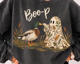 May include: A charcoal grey mineral-washed crewneck sweatshirt featuring a graphic of a mallard duck and a ghost covered in an autumn leaf pattern. The text "Boo-p" is printed in white above the figures, which are surrounded by tall grass.