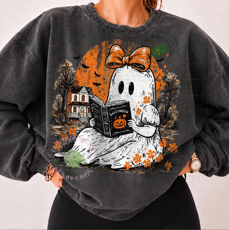 Op de afbeelding: Een antracietgrijze sweater met ronde hals en een afbeelding van een witte geest met een oranje strik, die een boek leest met de titel Halloween en een pompoenillustratie. De achtergrond toont een grote oranje maan, een huis en bomen.