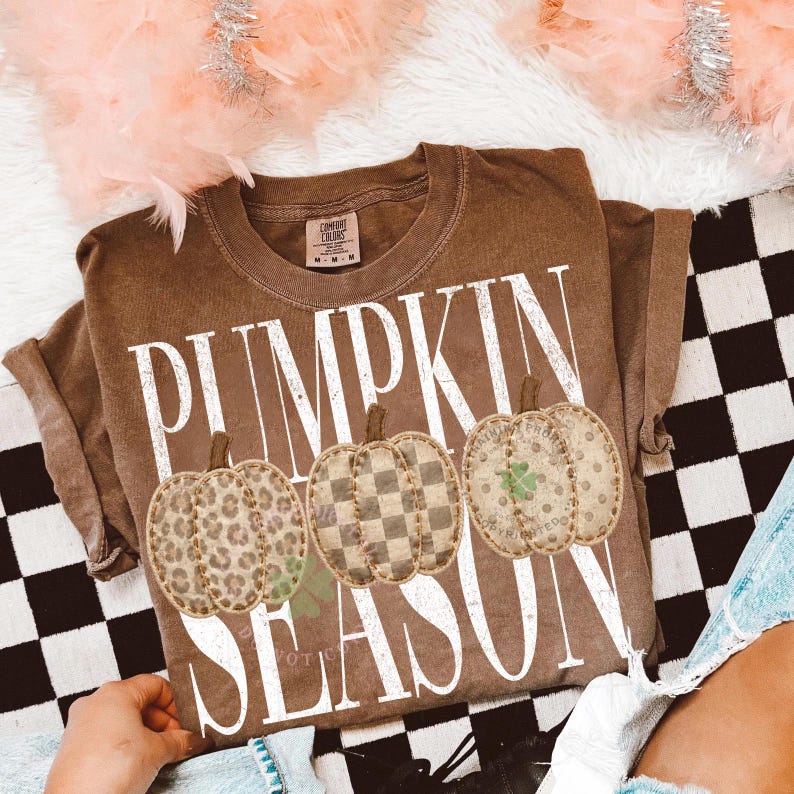 May include: A brown short-sleeve t-shirt featuring the white text PUMPKIN SEASON. The design includes three pumpkins with different patterns: one with a leopard print, one with a checkered pattern, and one with a polka dot print and a clover.