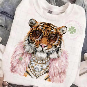 May include: White sweatshirt featuring a tiger wearing leopard print sunglasses, a pink feather boa, and a diamond necklace. The tiger illustration has a detailed design. The sweatshirt has the text "LOVERSEDIGITAL" and "NOT COPY".