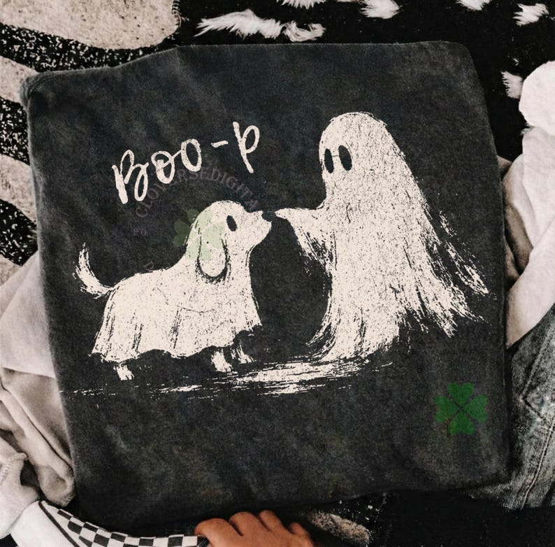 May include: A dark charcoal gray t-shirt featuring a white distressed graphic of a ghost and a dog wearing a ghost costume. The text "BOO-p" is printed in white above the figures. A small green four-leaf clover icon is visible in the bottom corner.
