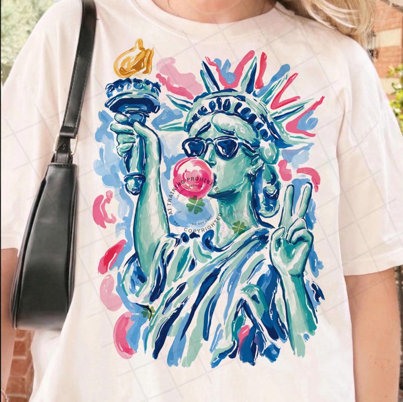 May include: Off-white t-shirt featuring a colorful illustration of the Statue of Liberty wearing sunglasses and blowing a bubblegum bubble. The Statue of Liberty is depicted in shades of blue and green, with pink and blue accents. The design includes the text "ALL RIGHTS RESERVED".