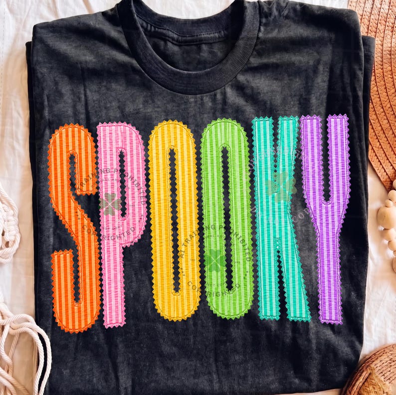 以下が含まれることがあります： 黒の半袖Tシャツで、大きくカラフルな縦縞模様の文字で「SPOOKY」とプリントされています。各文字には特徴的なスカラップ状の縁取りがあり、オレンジ、ピンク、イエロー、ライムグリーン、ティール、パープルの順で並んでいます。