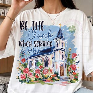 May include: White t-shirt featuring a watercolor illustration of a church with a blue steeple and a cross. The shirt has the text "BE THE Church WHEN SERVICE is over" in black and blue. Floral accents surround the church.