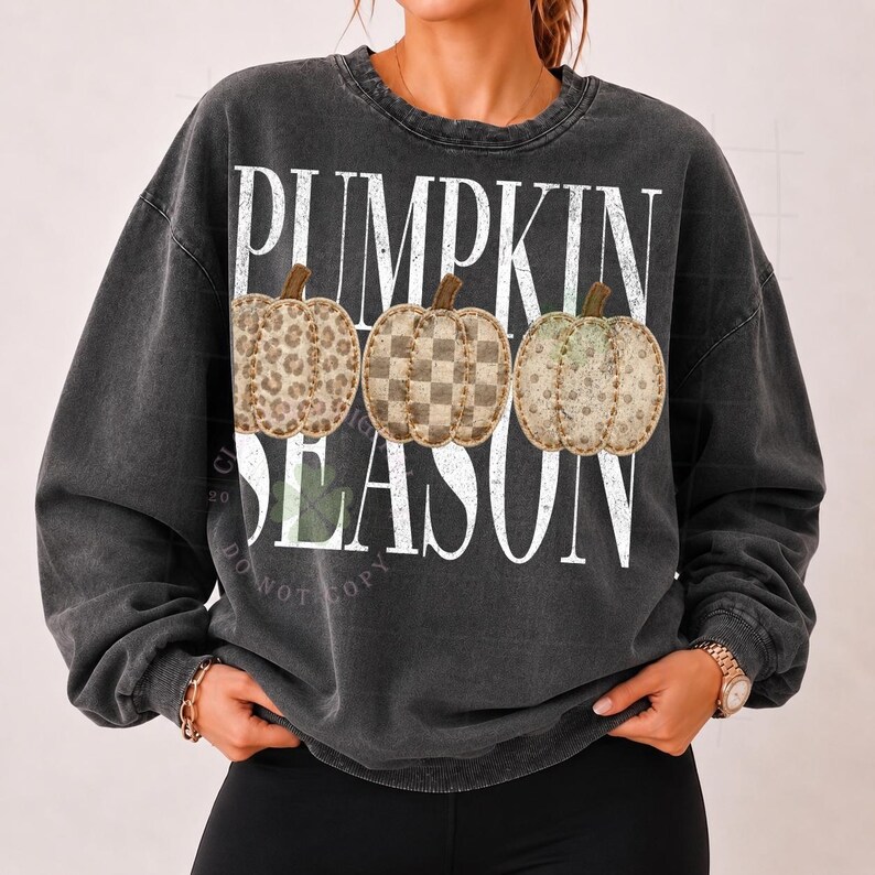 May include: A charcoal grey crewneck sweatshirt featuring the white text PUMPKIN SEASON. The design includes three illustrated pumpkins with distinct patterns: a leopard print, a checkered pattern, and a solid tan color with brown stems.