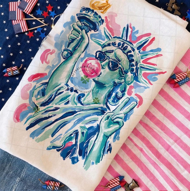 May include: A white fabric with a colorful illustration of the Statue of Liberty wearing sunglasses and blowing a bubblegum bubble. The Statue of Liberty is holding a torch and making a peace sign. The background includes a blue and white star-patterned fabric and a pink and white striped fabric.